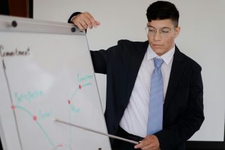 Young professional in eyeglasses presents data on a whiteboard during an office meeting.